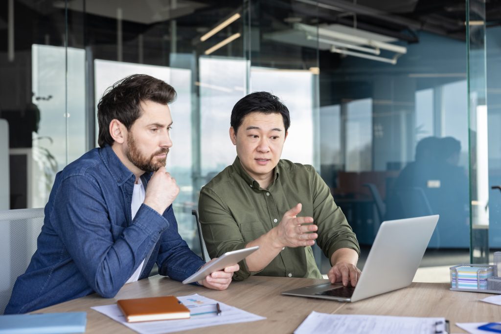 Diverse business professionals collaborating on laptop in modern office | Quest Mindshare Business professional sharing expertise, a key driver of B2B survey response rates
