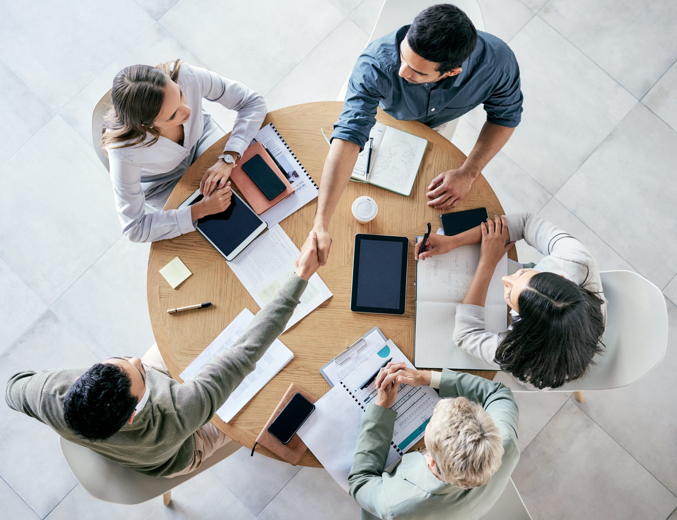 Meeting, handshake and overhead with a business team sitting around a table in the office at work