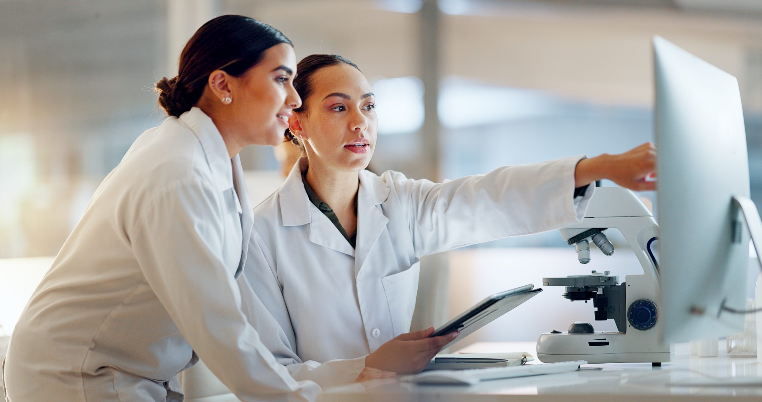 Scientist and colleague reviewing research data on a tablet and computer in a lab