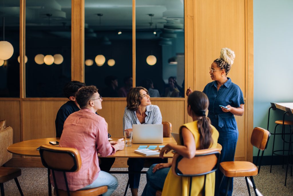 Diverse group of colleagues discussing ideas around a small conference table | Quest Mindshare Researcher defining hard-to-reach audiences for niche audience research