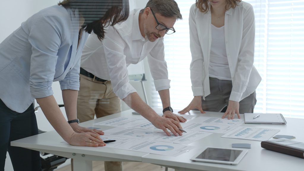 Business professionals collaborating around a modern office table reviewing charts and reports brainstorming strategy and data driven decisions to drive growth and team performance | Quest Mindshare Market research project management checklist for online fieldwork