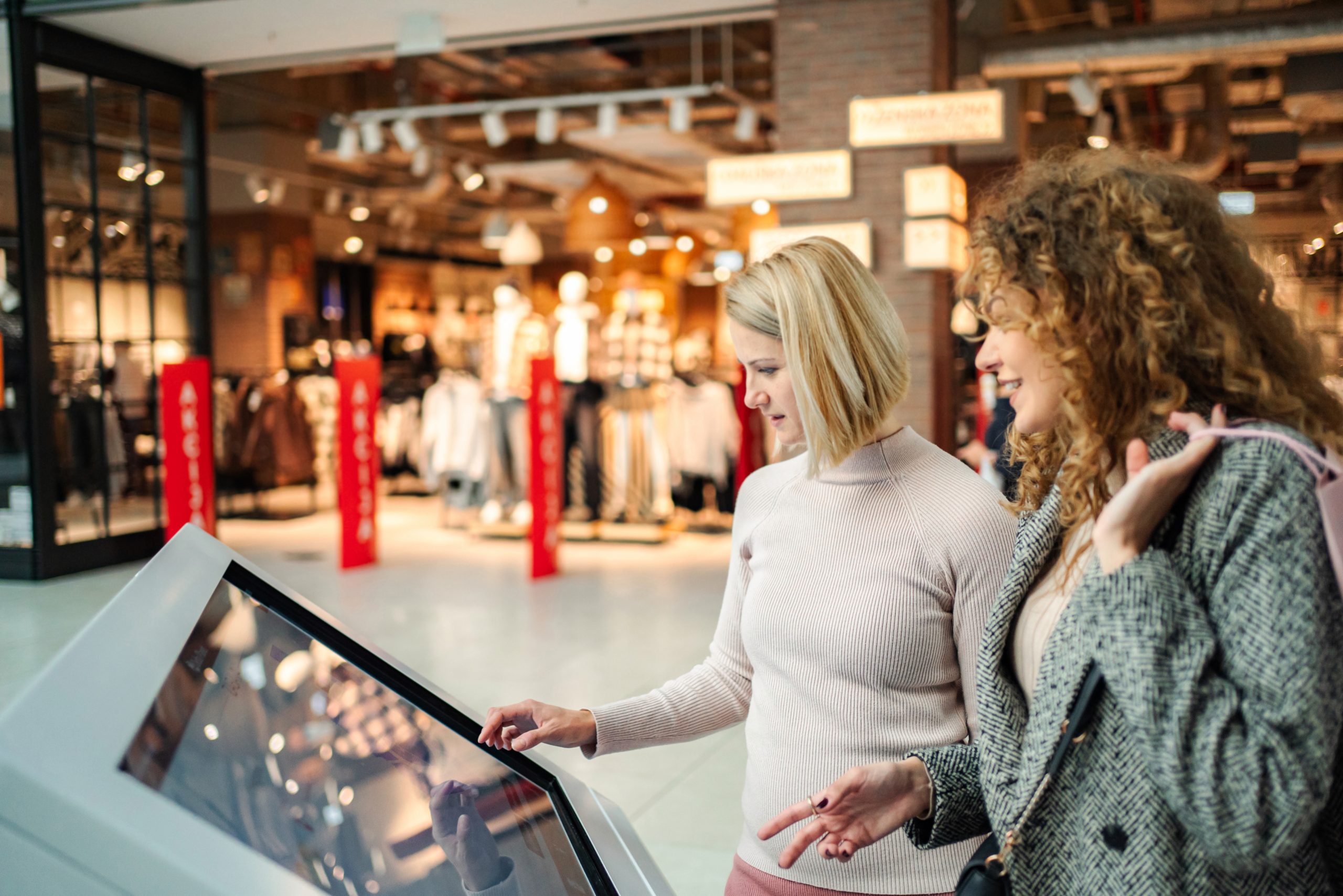 Two shoppers using a touchscreen kiosk in a shopping mall