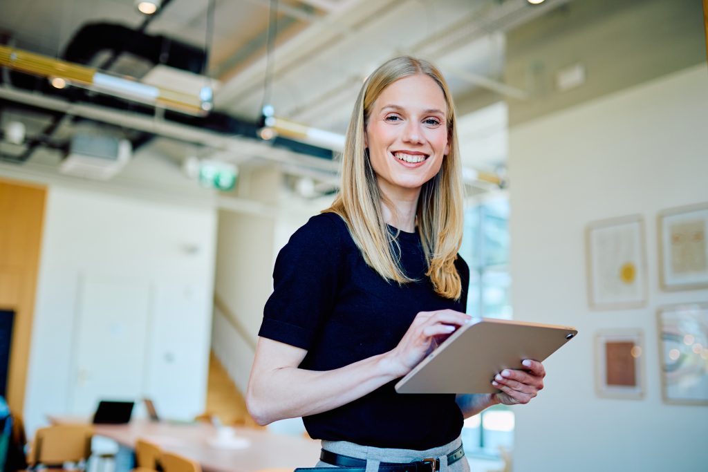 Young business woman smiling using a digital tablet for work in a modern office environment Professional female employee at work | Quest Mindshare Researcher writing screening questions for B2B survey screening