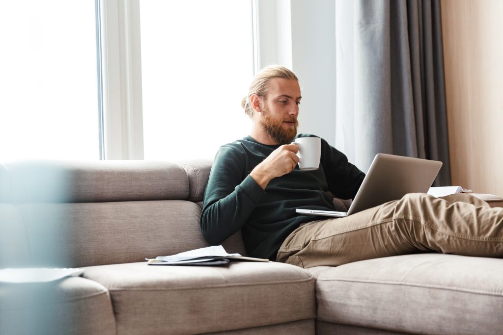 Concentrated young bearded man sitting in home using laptop computer | Quest Mindshare Job seeker browsing online job boards, showing the job search trends behind today's hiring challenges
