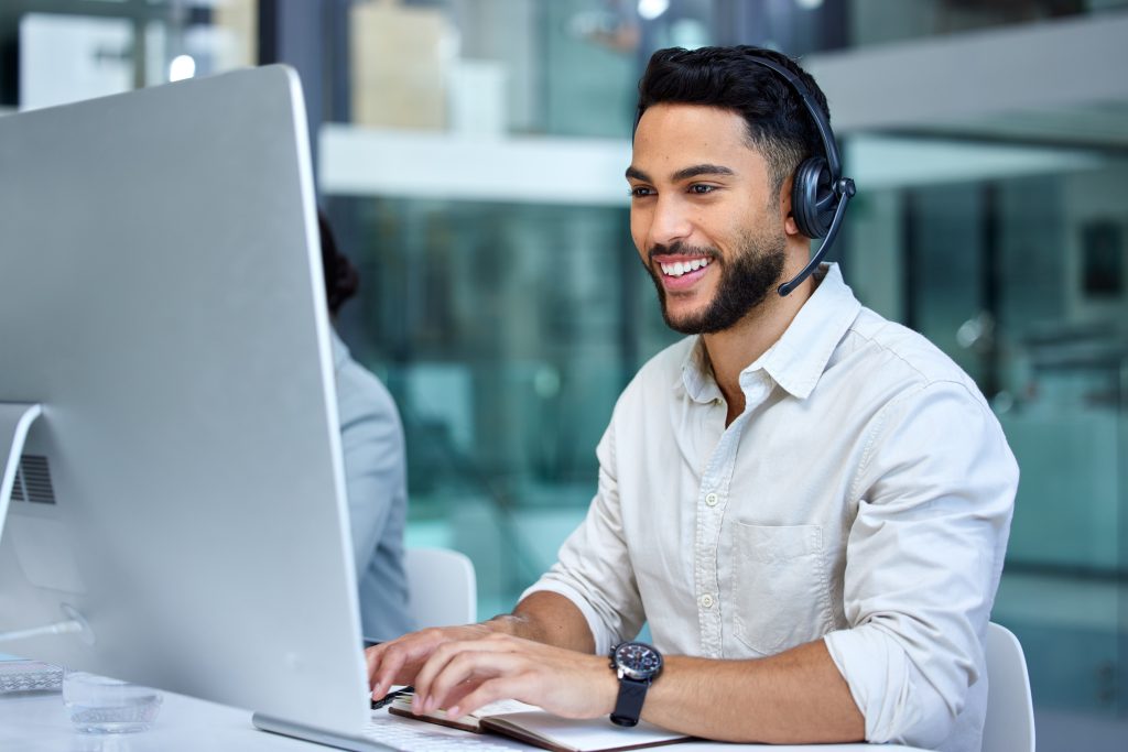 Business man call center and web support communication at a computer in a office Phone conversation smile and male worker with contact us crm and customer service job in a consulting agency | Quest Mindshare Project manager responding to a client, showing great customer service in market research